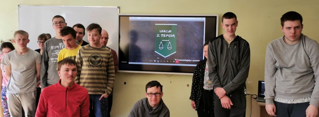 grupa uczniów stoi obok monitora na którym jest wyświetlone zielone logo 