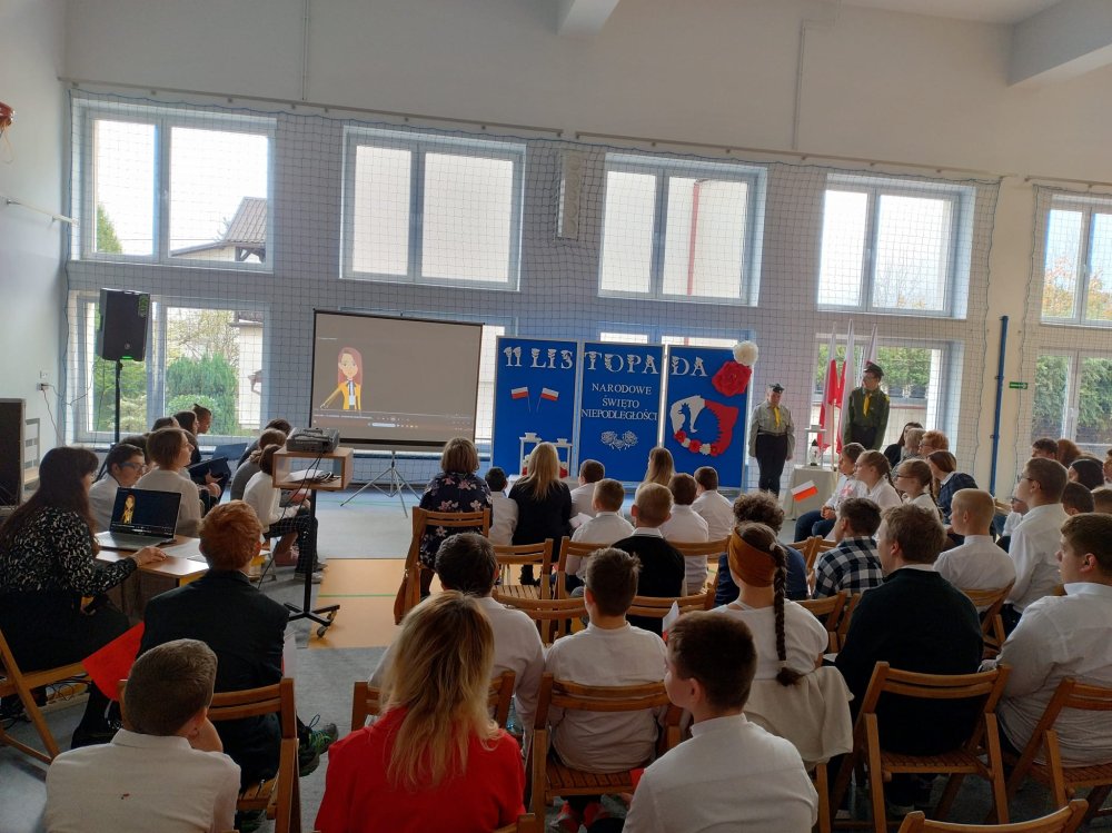 Na zdjęciu znajdują się uczniowie siedzący na sali gimnastycznej i oglądający film na temat odzyskania niepodległości przez Polskę.