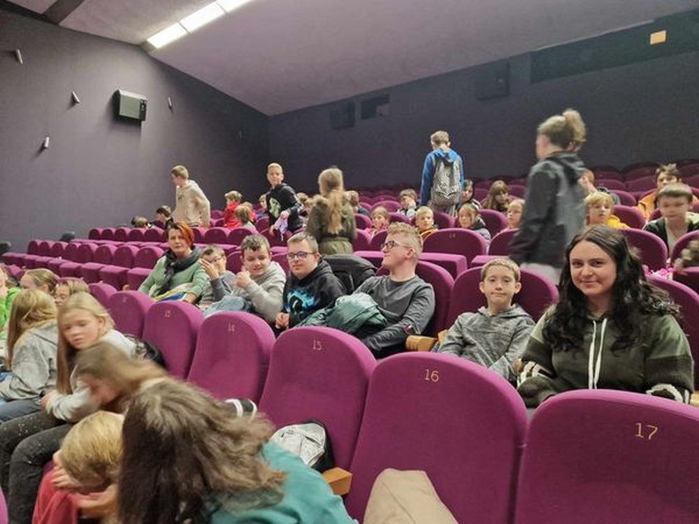 Na zdjęciu znajdują się uczniowie wraz z nauczycielką siedzący w sali kinowej.