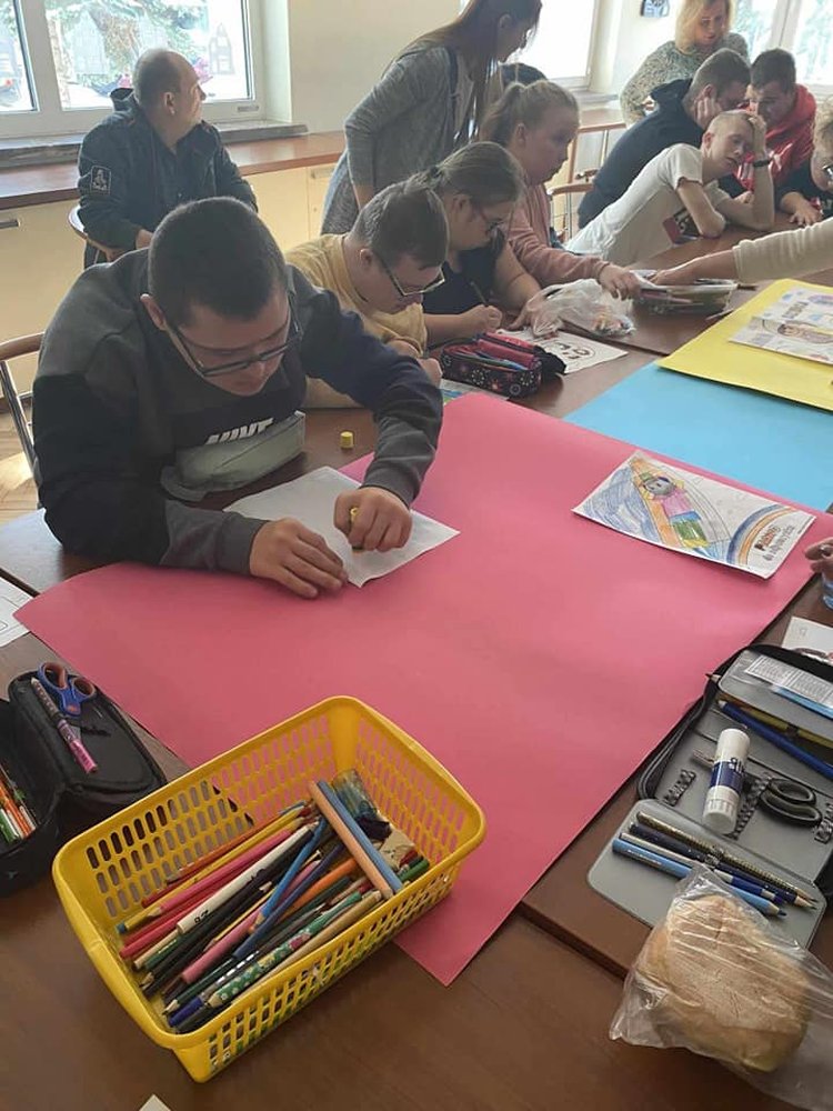 Uczniowie siedzą przy stolikach i kolorują obrazki do plakatów.