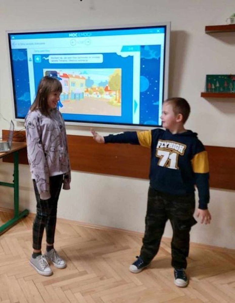 Uczeń i uczennica stoją przy tablicy interaktywnej i odgrywają scenkę.