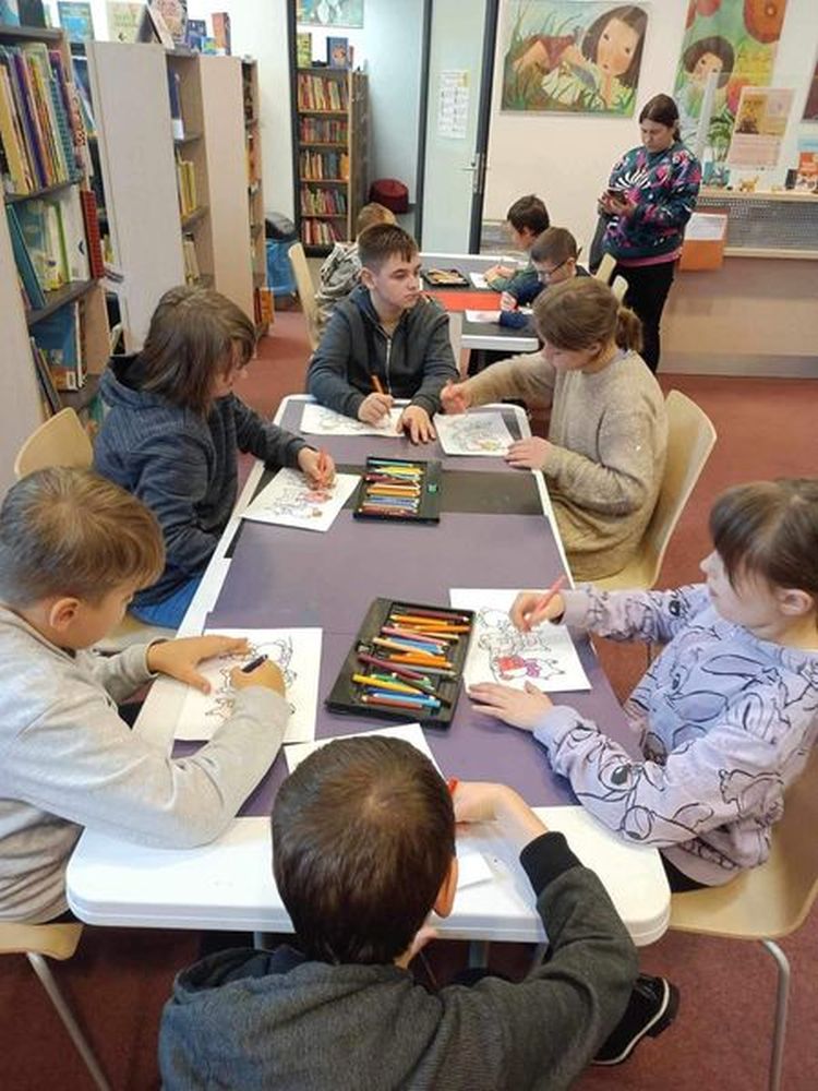 Zdjęcie przedstawia uczniów siedzących przy stolikach i kolorujących obrazki.