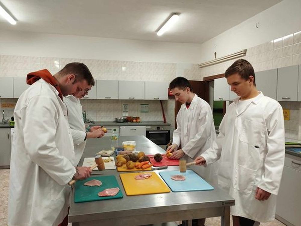 Uczniowie przebrani w fartuchu przygotowują obiad w pracowni kucharskiej.