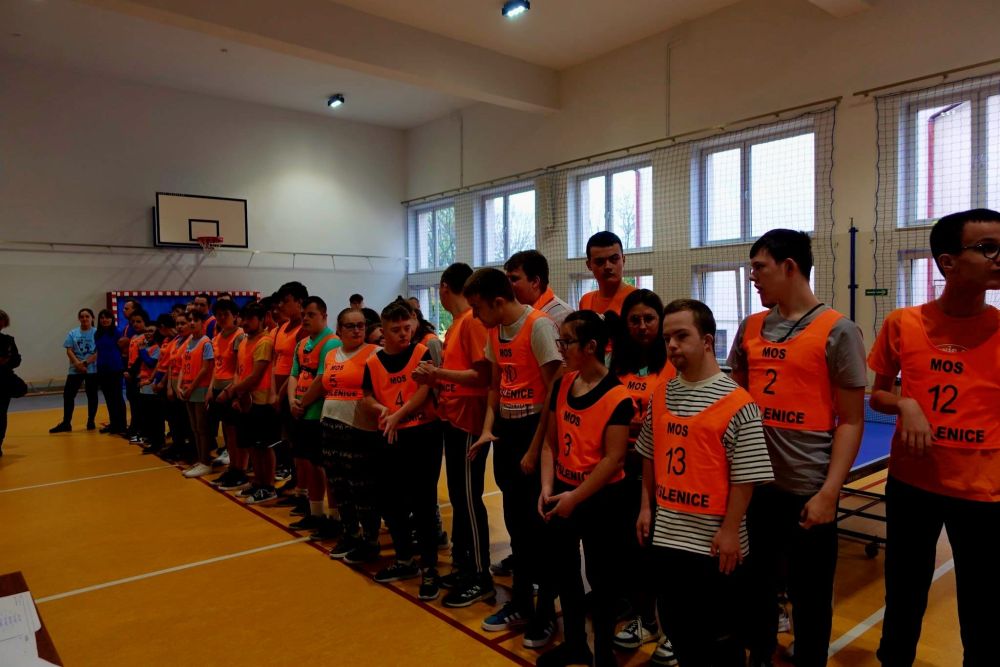 Uczestnicy turnieju stoją w 2 rzędach w pomarańczowych koszulkach.