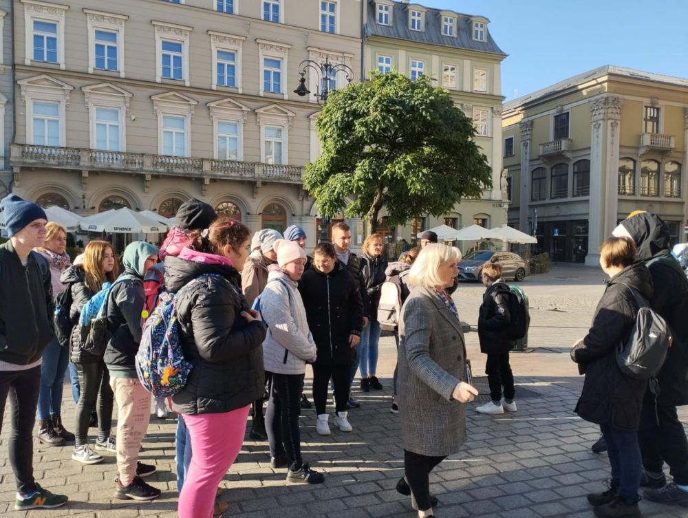 Uczniowie podczas wycieczki do Krakowa spacerują po Rynku i słuchają legend krakowskich.