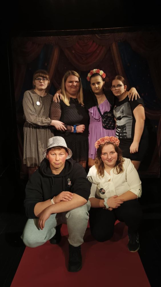 Grupa uczniów, 4 uczennice stoją, uczeń i uczennica kuca. Wokół nich czarne tło.