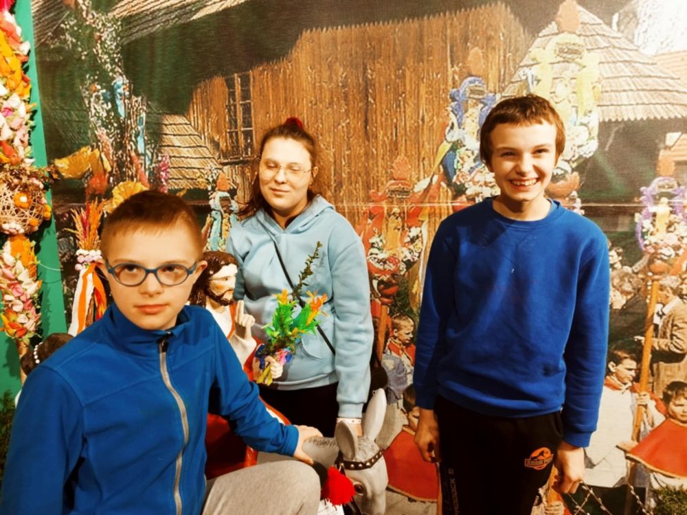 2 uczniów i 1 uczennica stoją w Muzeum Niepodległości podczas warsztatów wielkanocnych, wokół nich jest bardzo kolorowo, uczennica trzyma w ręce palmę wielkanocną.