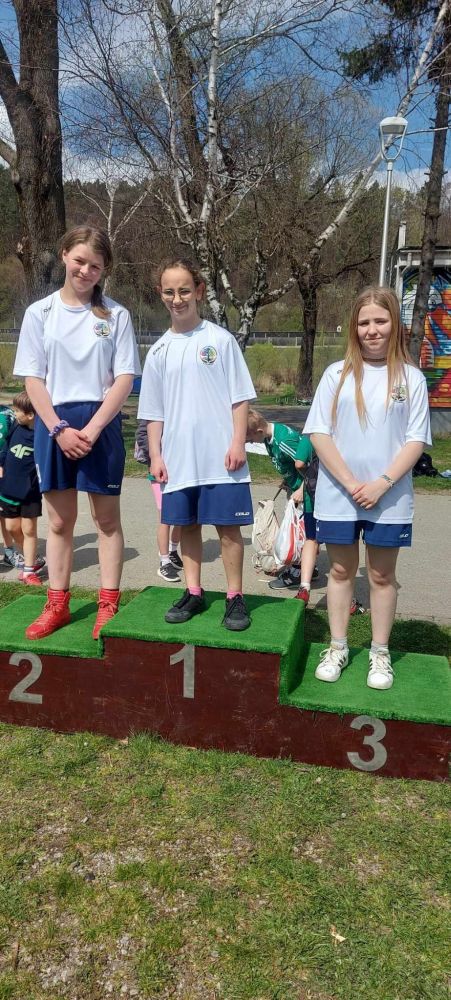 3 dziewczyny ubrane w białe stroje stoją na podium, na 1,2 i 3 miejscu w kategorii dziewczyn.