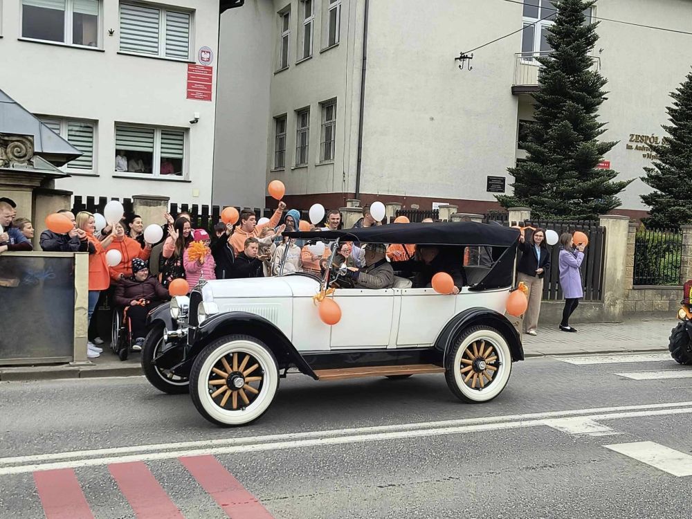 Kilka zdjęć, na których uczniowie stoją pod szkołą na chodniku z pomarańczowymi balonami w ręku i machają do przejeżdżającego auta, ubranego również w pomarańczowe balony.