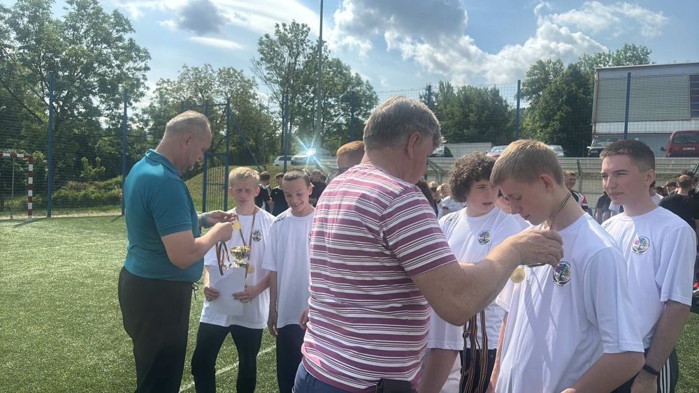 2 panów zakłada na szyję medale uczniom, którzy brali udział w zawodach.