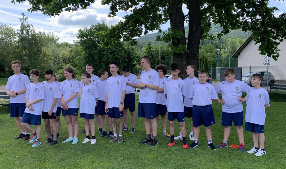 Grupa uczniów w białych strojach sportowych stoi na trawie.