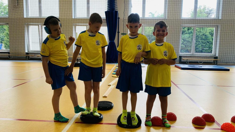 4 chłopców ubranych w żółte stroje sportowe stoi na sali gimnastycznej w rzędzie. 
